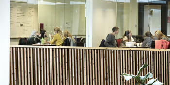 Billedet er taget udenfor to grupperum, hvor væggene er lavet af glas, så man kan se elever sidde i begge rum. Der sidder fire elever i hvert rum og arbejder og snakker. 